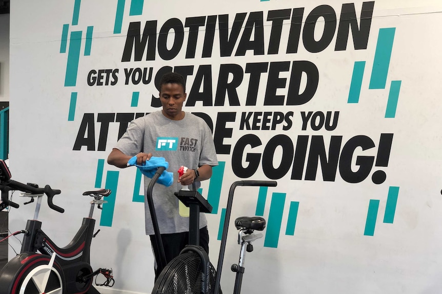 A man spraying an exercise bike with disinfectant in a gym