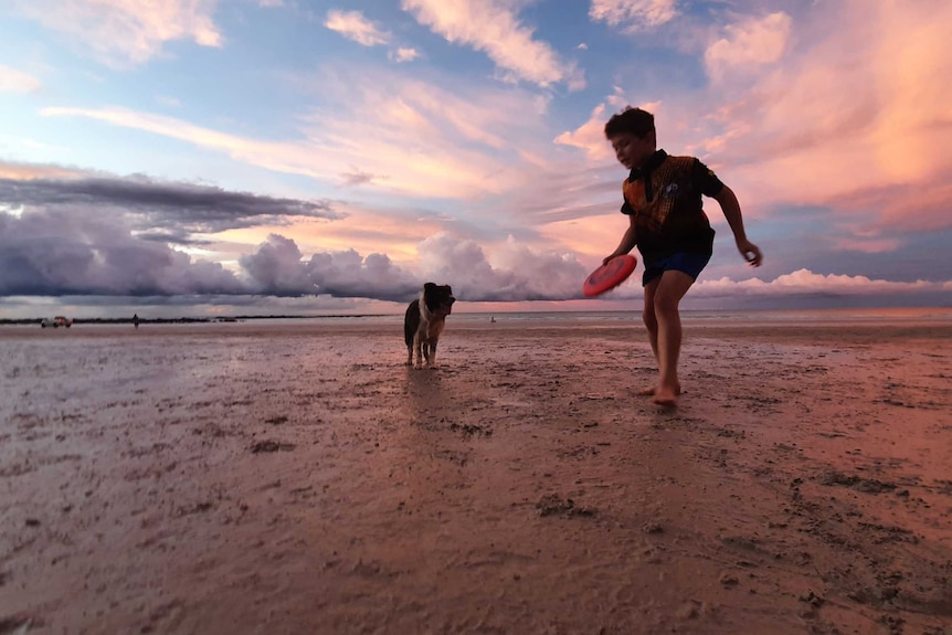 A boy throws frisbee to his dog in Broome as storm rolls in