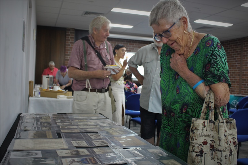 An elderly lady looks at a table of historical artifacts 