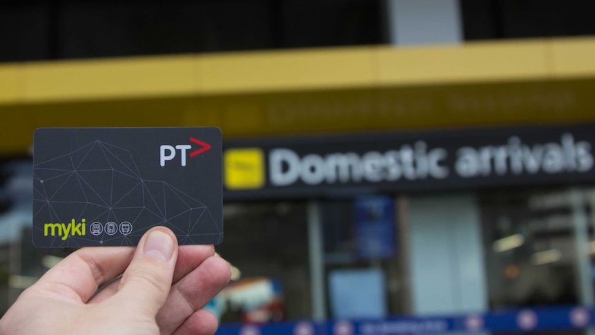 A hand holds a myki card, sign in background reads 'Domestic Arrivals'