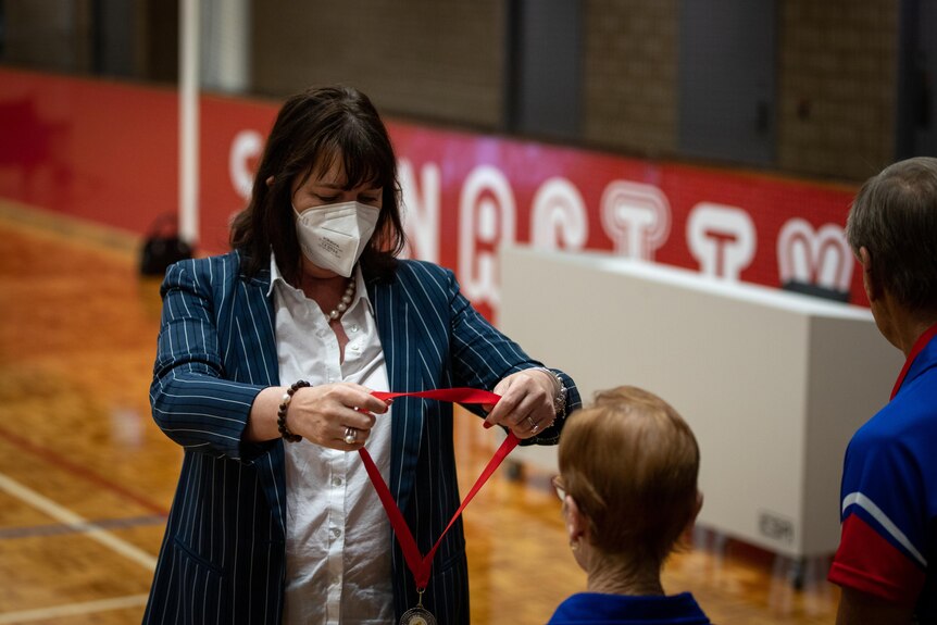 A woman with a mask on presents a medal.