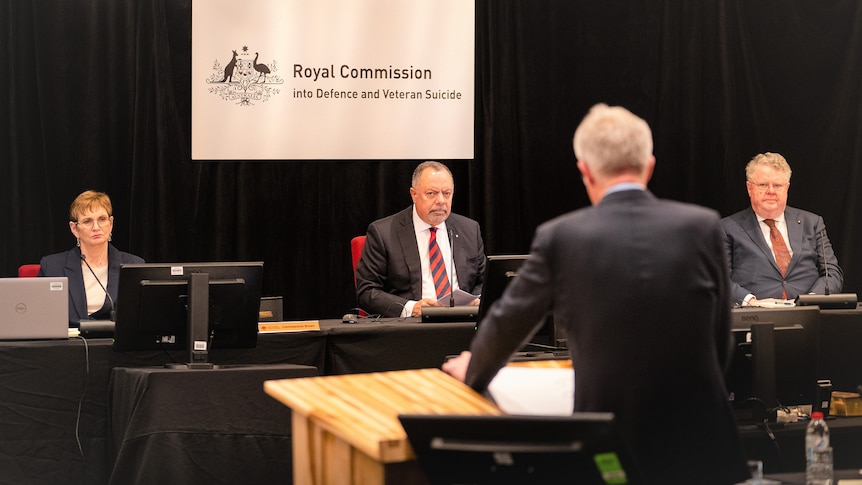 Three people sit facing a speaker who has his back turned to the camera.