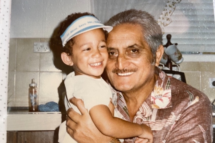 Old photo of a small boy wearing a white cap being held up by a middle-aged man with grey hair and a moustache 