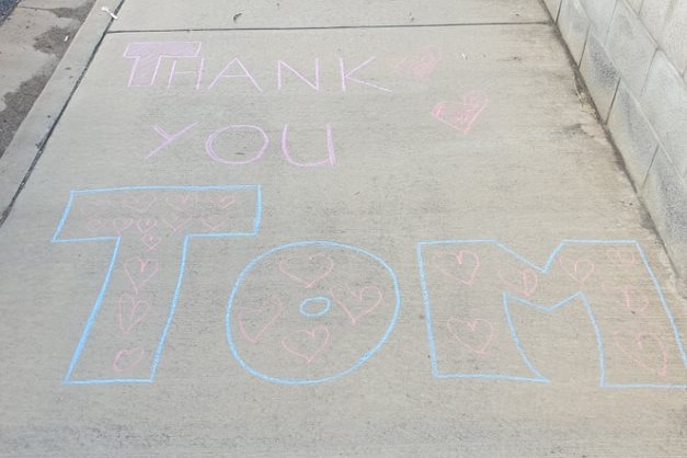 'Thank you Tom' written in pink and blue chalk on a footpath. 