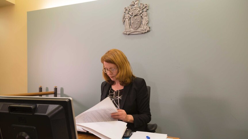 Magistrate Pauline Spencer reads papers while sitting at a bench inside a courtroom.