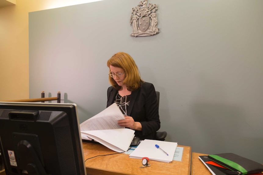 Magistrate Pauline Spencer reads papers while sitting at a bench inside a courtroom.