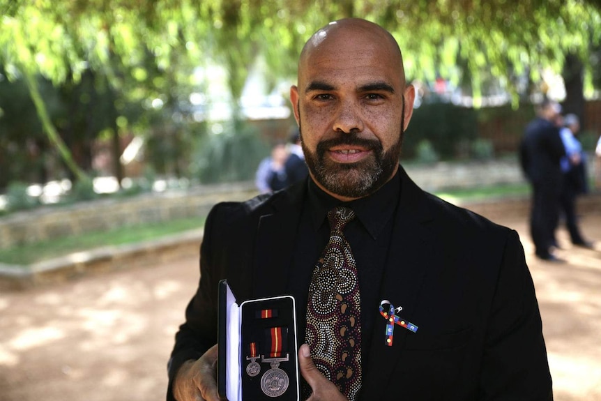 Nathan Hansen outside under trees holding a medal.