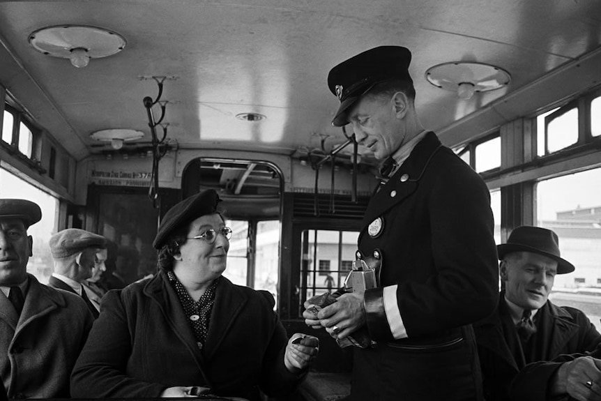 A London bus conductor collects a fare from a woman. Black and white photo.
