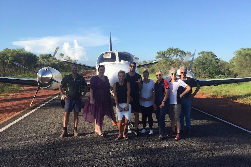 Eight people stand posing for a photo in front of a light plane on Great Northern Highway.