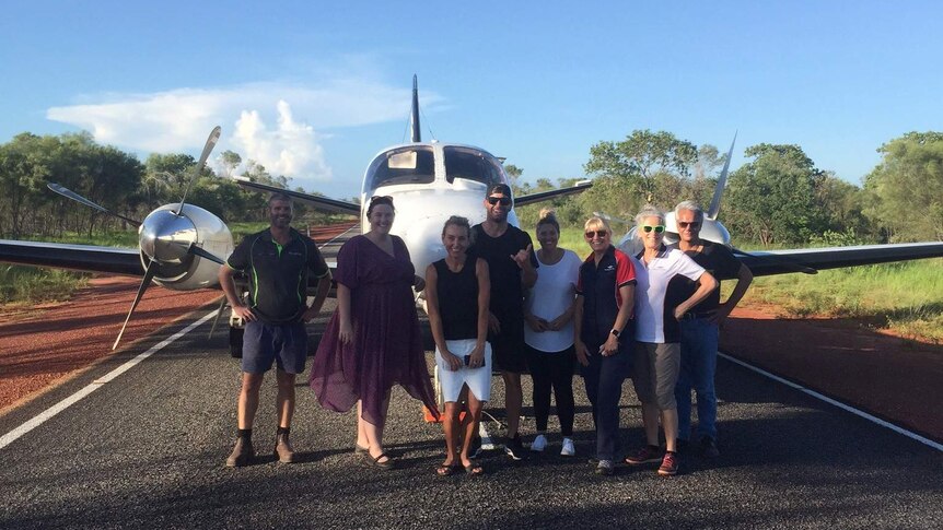 Eight people stand posing for a photo in front of a light plane on Great Northern Highway.