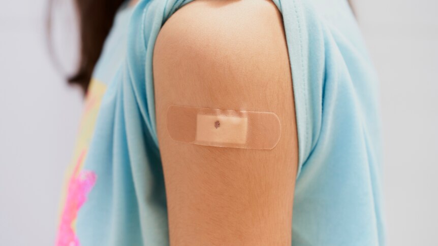 A small bandage covers the vaccine injection site on the arm of young girl.