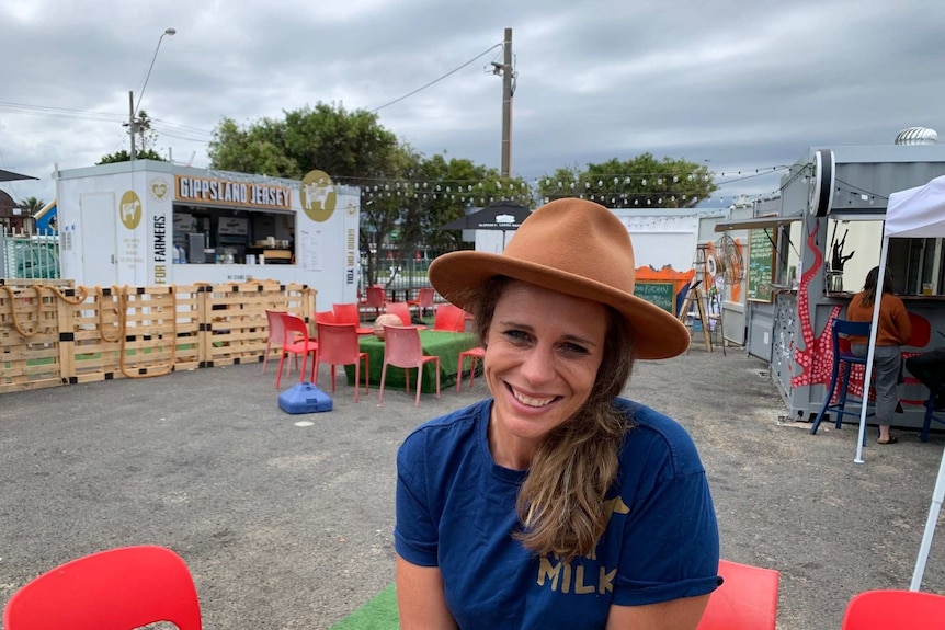 Smiling young women in hat poses in front of food truck courtyard.