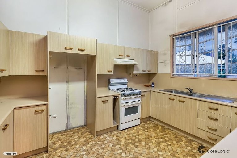 An empty kitchen with brown, dated vinyl and fibro on the wall.