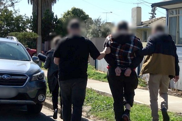 Three people lead a man in handcuffs to a car.