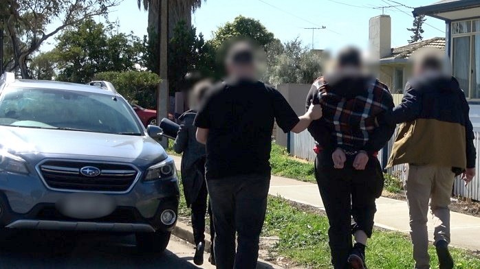 Three people lead a man in handcuffs to a car.