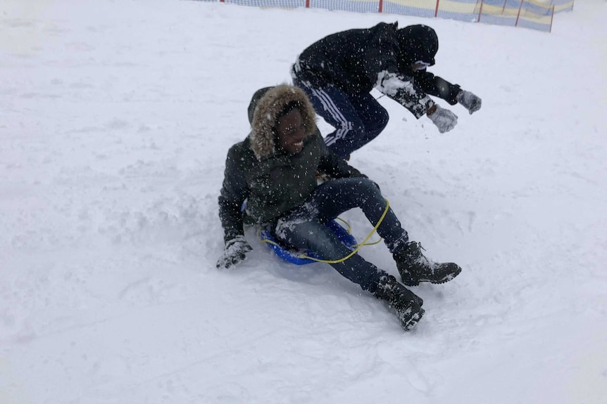 Young people from refugee backgrounds try tobogganing on their first trip to the snow.