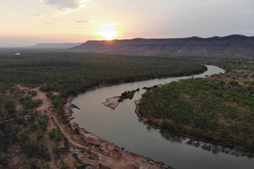 a winding river with a hill and sunset in the background.