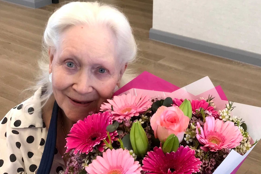 An older lady smiling with beautiful flowers.