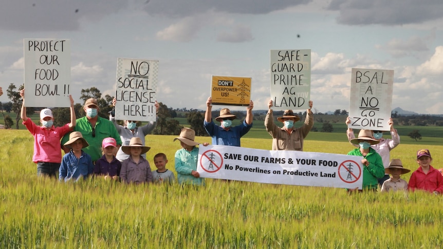 Farmers stand in a paddock holding up placards reading "Safeguard prime ag land" and "We will fight for our land".