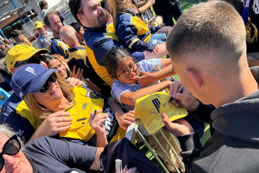 a central coast mariners player signs autographs for fans after winning the mens a-league grand final