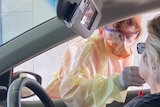 A nurse takes a swap from a patient inside a car at a fever clinic.
