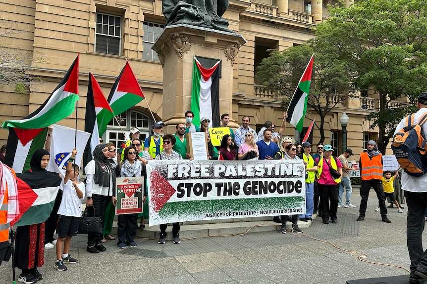 dozens of people waving palestinian flags and holding a sign saying free palestine stop the genocide