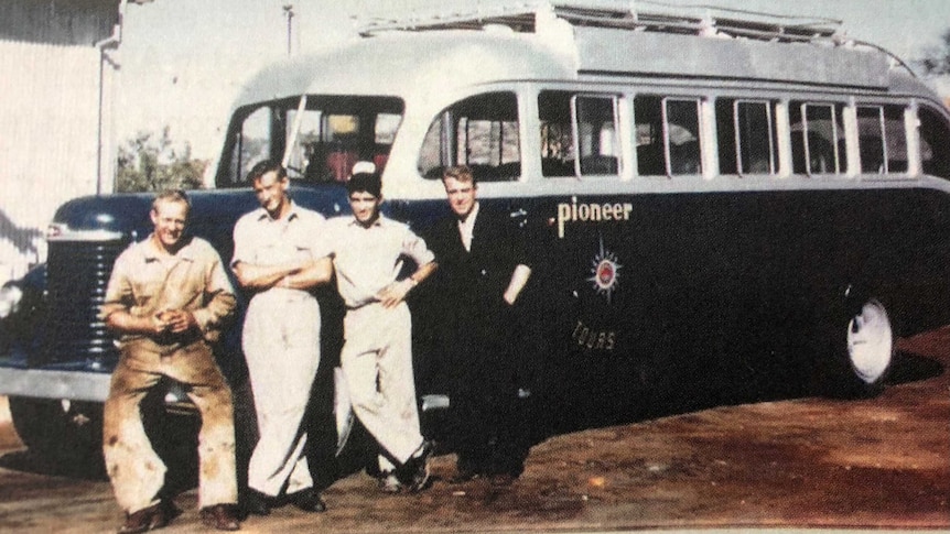 Four men stand next to a Pioneer tour bus ready to depart for Uluru.