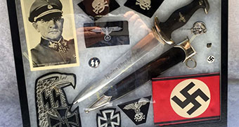 A framed collection of Nazi artefacts, including dagger, spear blade, badges, cloth patches and print of Third Reich Officer.