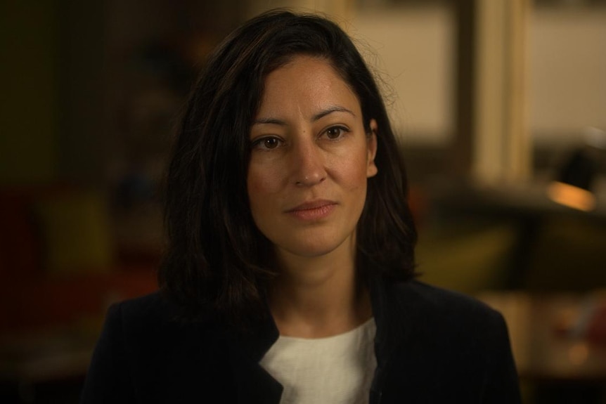 A woman with mid-length dark hair looks serious as she is interviewed for television.