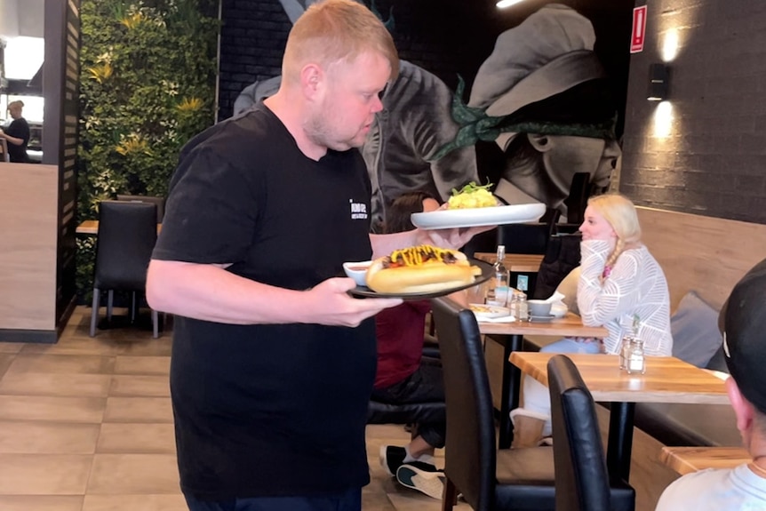 A man carries two plates of food in an indoor cafe