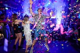 Young people dance in nightclub with confetti in the air.