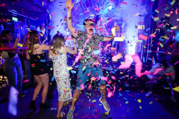 Young people dance in nightclub with confetti in the air.