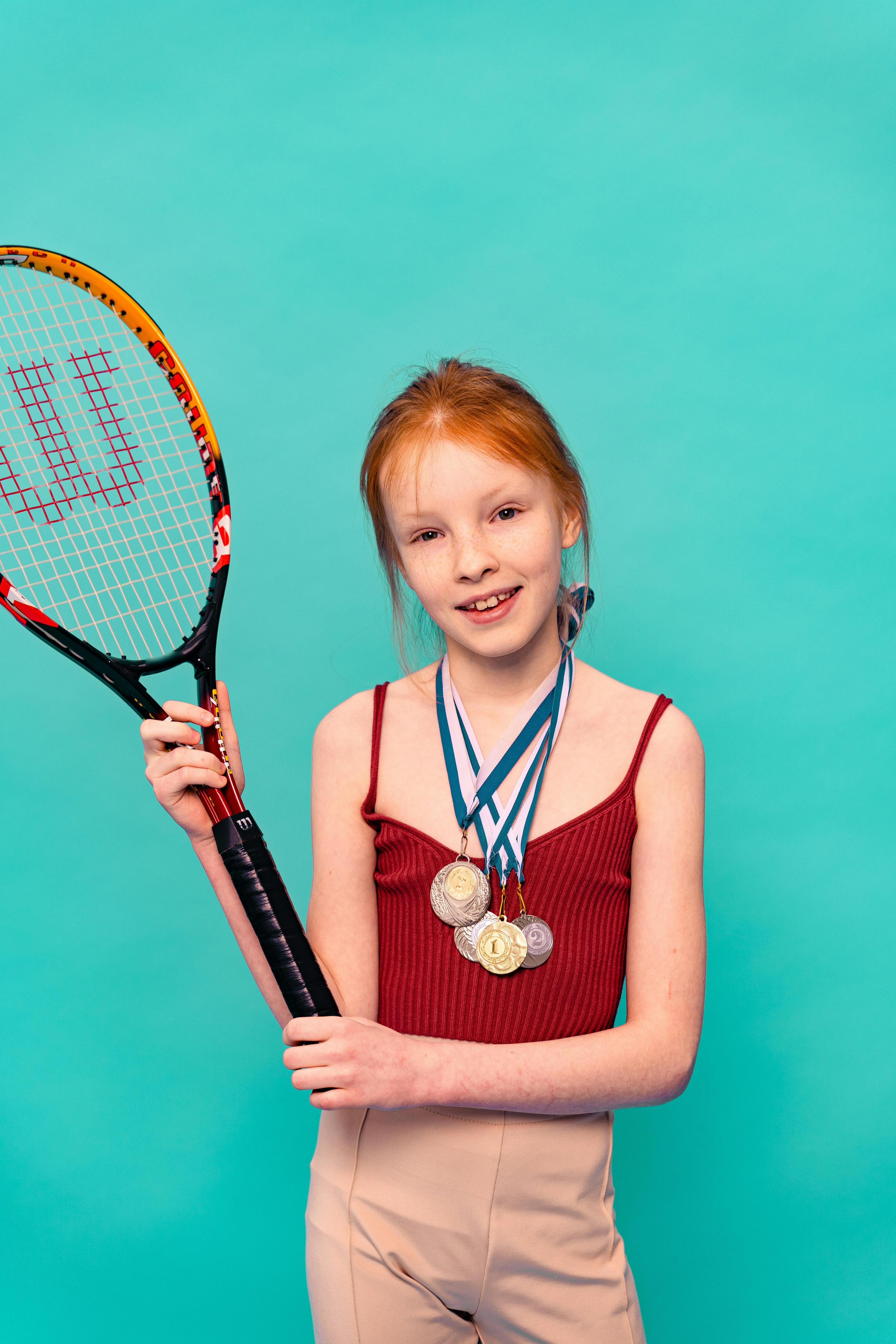 Young girl with long red hair holding a tennis racquet with medals around her neck