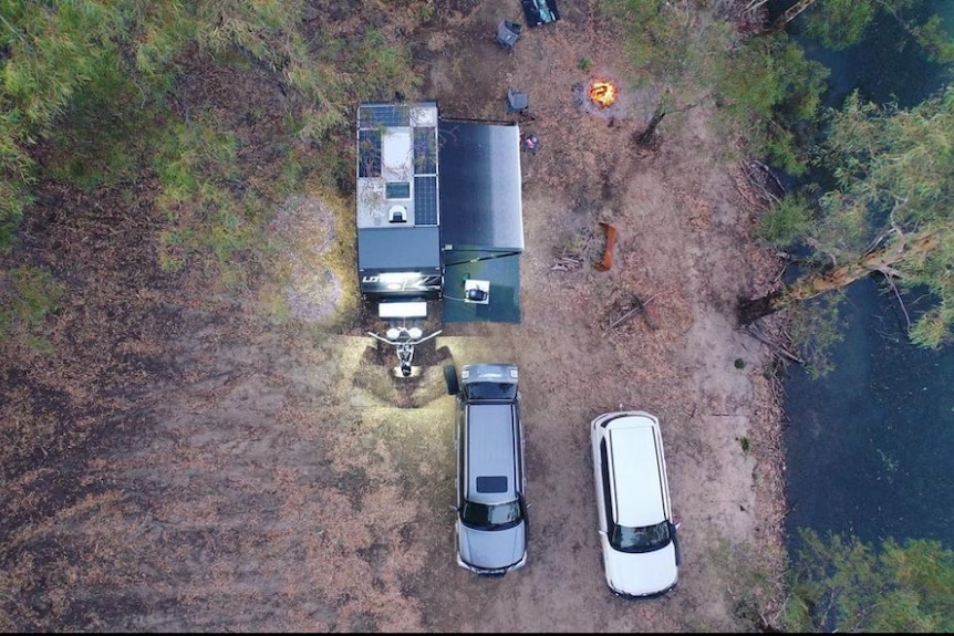 Bird's eye view of two cars and a caravan with an annexe next to a river. 