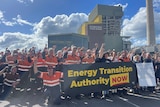 Dozens of people standing outside a power station holding a banner calling for an energy transition authority to be established.