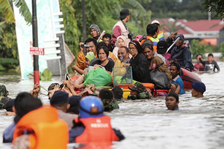 Dozens of people sit upon a raft and are making their way through floodwaters.