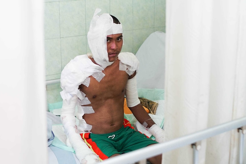 Anggi Aji Pangetsu sits on a hospital bed wrapped up in bandages