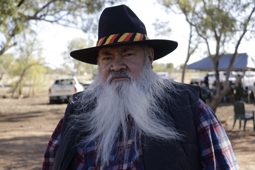 WA Senator Patrick Dodson wearing a hat and flanette shirt and vest, looking serious. 