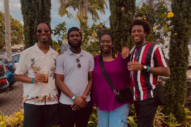 a woman stands smiling at the camera with her three adult sons