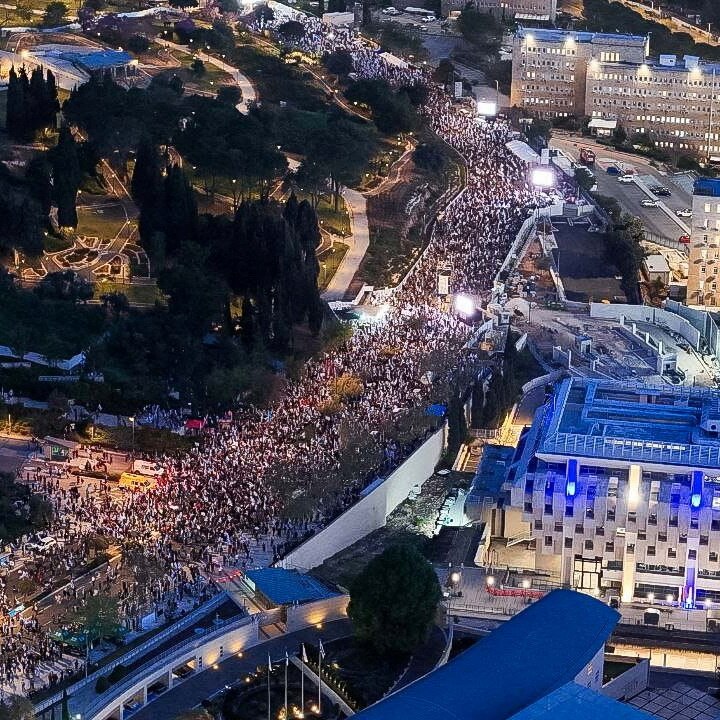 A drone image of a street filled with tens of thousands of protesters in front of the Israeli parliament at night time