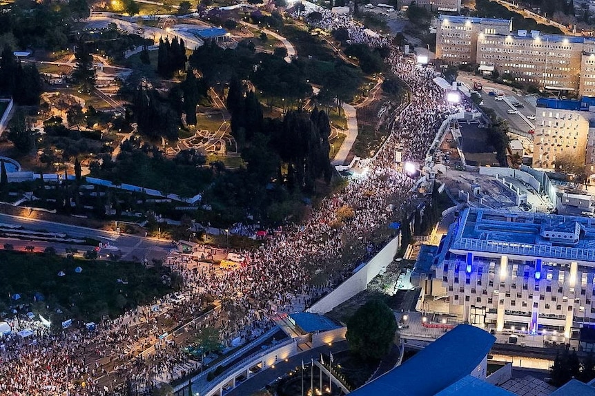 A drone image of a street filled with tens of thousands of protesters in front of the Israeli parliament at night time