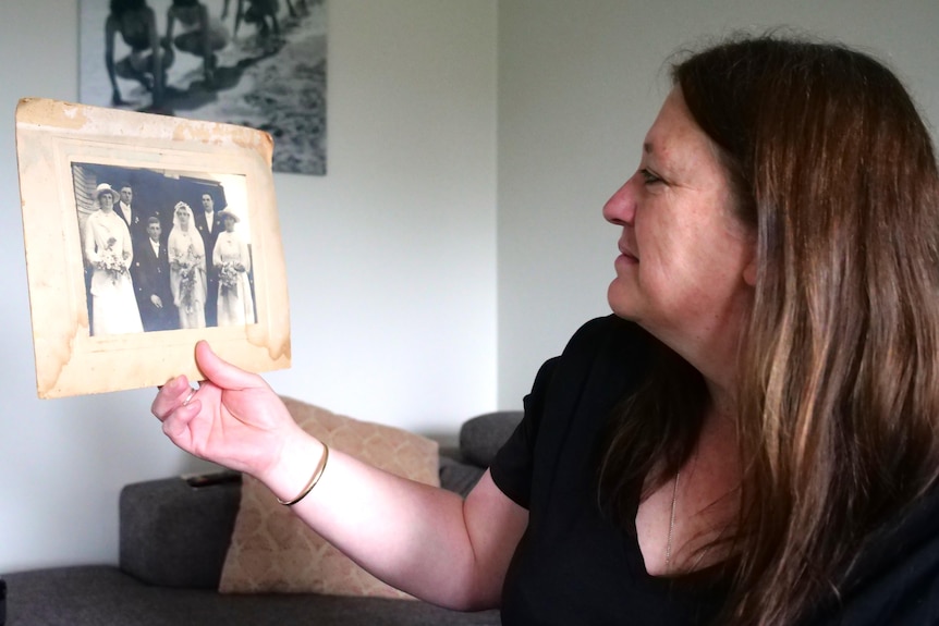 A woman holds up an old wedding photo and looks at it 