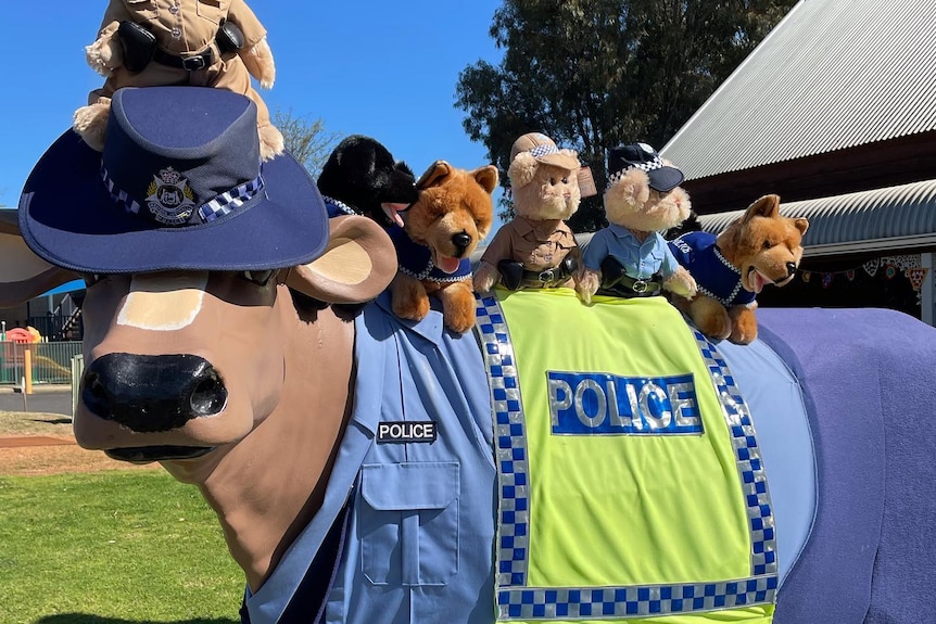 Cow statue with police uniform and teddies sitting on top.