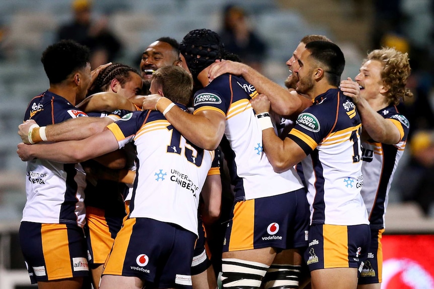 Brumbies Super Rugby AU players embrace as they celebrate a try against the Melbourne Rebels in Canberra.