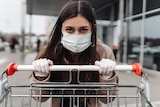 A young woman wearing a surgical mask pushing a trolley