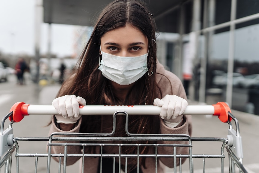 A young woman wearing a surgical mask pushing a trolley.