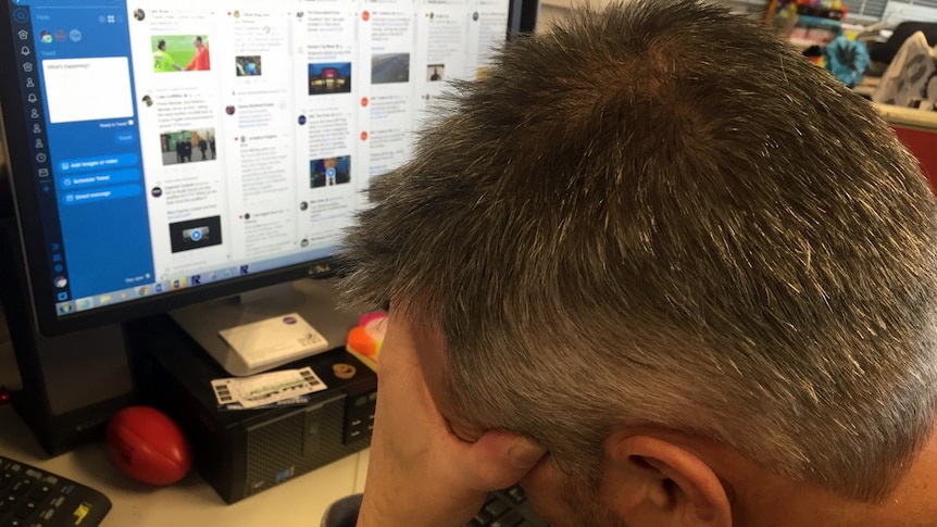 Distressed man has his head in his hands in front of his computer screen.