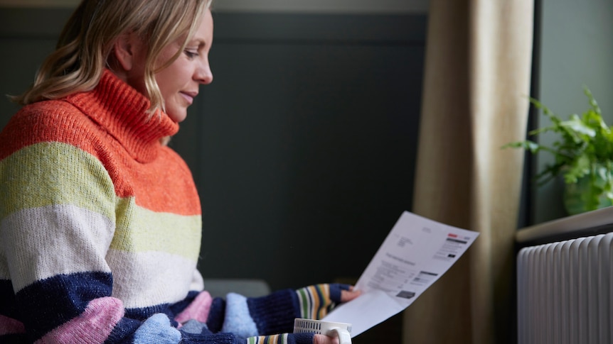 A woman in a warm pullover is looking at a utility bill
