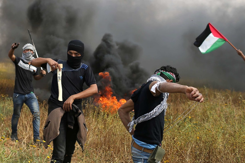 A man holds an axe as his companion prepares stones to throw at israeli troops