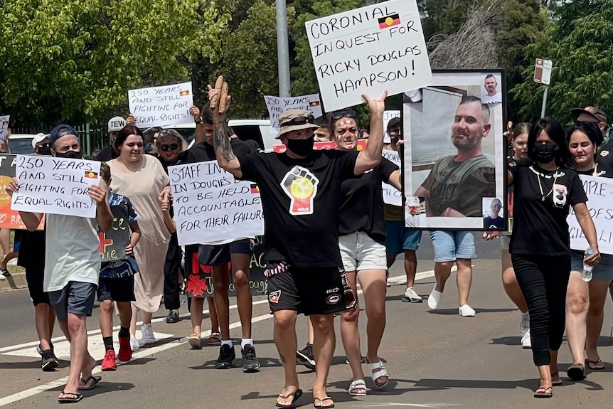 A group of people holding signs calling for justice and a large photograph of their family member